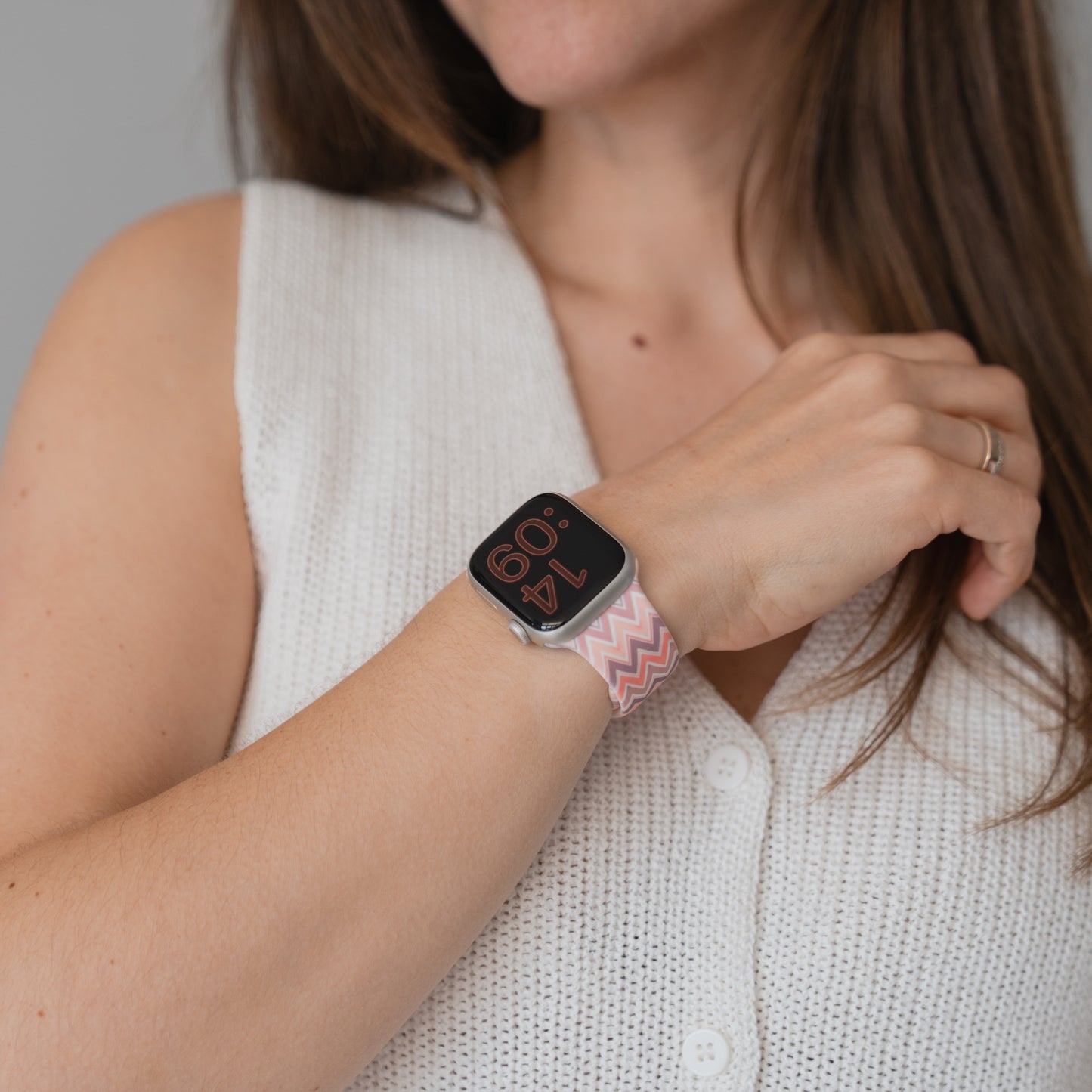 Eine Frau trägt ein weißes ärmelloses Oberteil und ein Arktisband Vintage Boho Apple Watch Armband mit einem rosa, sportlichen Silikonarmband an ihrem Handgelenk.