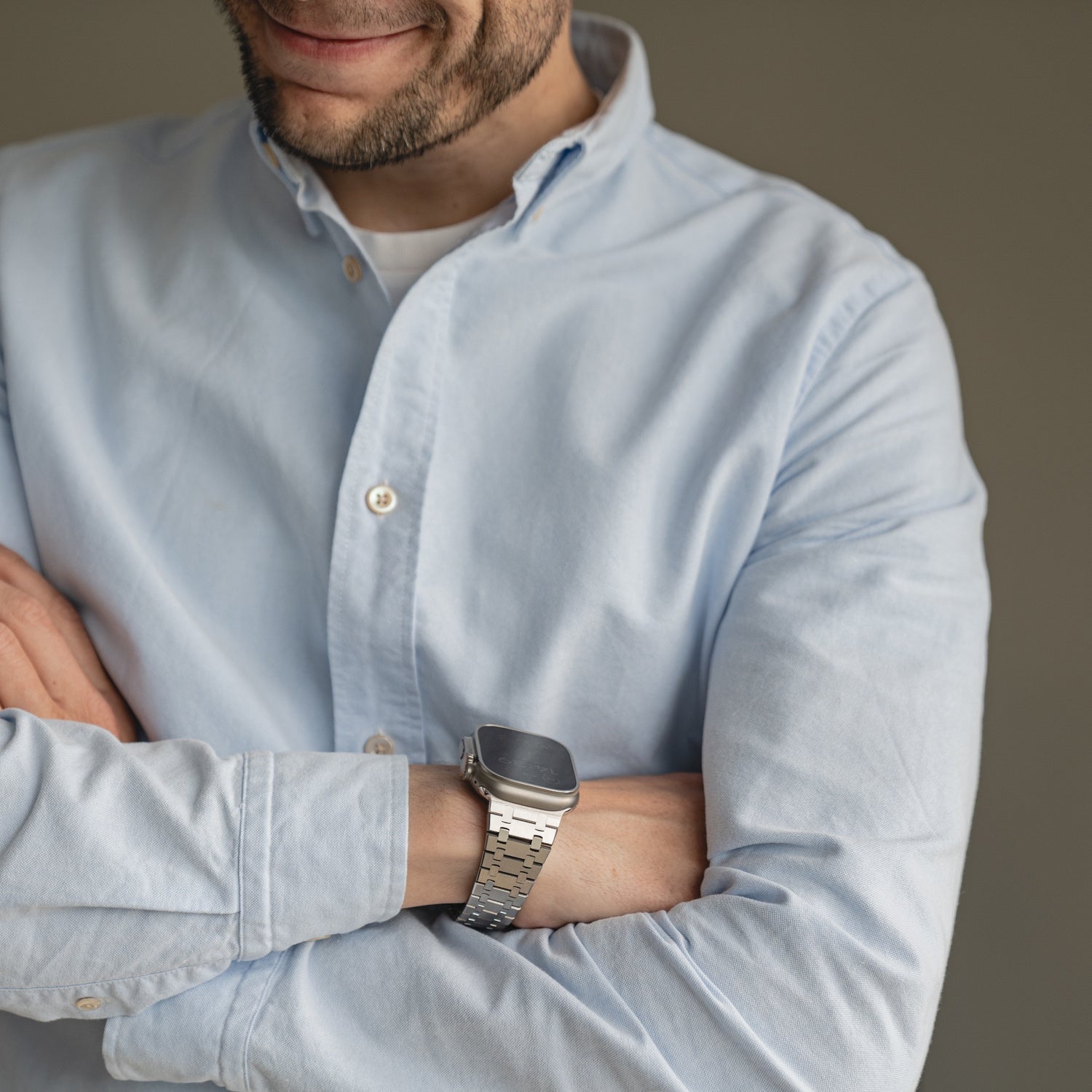 Mann in einem hellblauen Hemd mit Knöpfen, mit verschränkten Armen, leicht lächelnd, trägt das arktisband Edelstahlarmband „Symphony“ für die Apple Watch von arktisband.