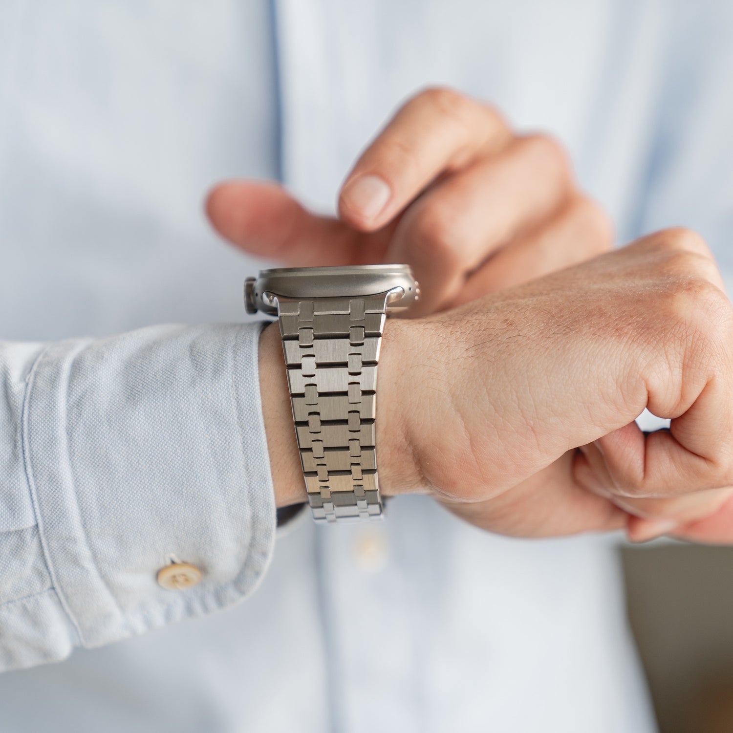 Nahaufnahme einer Person in einem hellen Hemd, die auf einem Arktisband-Edelstahlarmband „Symphony“ für die Apple Watch aus 316L-Edelstahl die Uhrzeit überprüft.