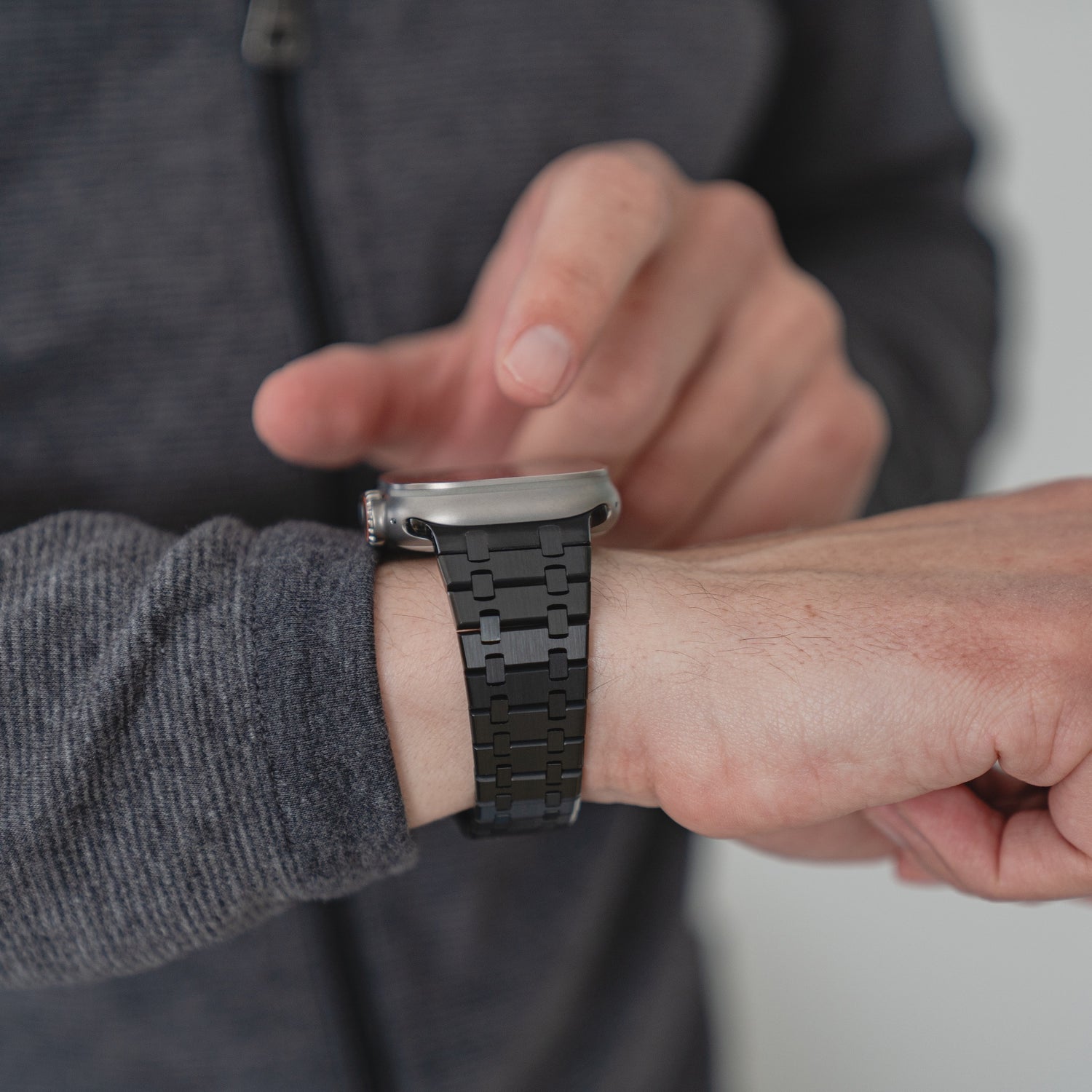 Eine Person in einer grauen Jacke tippt auf ein Arktisband Edelstahlarmband „Symphony“ für die Apple Watch mit einem schwarzen Butterfly-Verschluss aus chirurgischem Edelstahl 316L an ihrem Handgelenk.