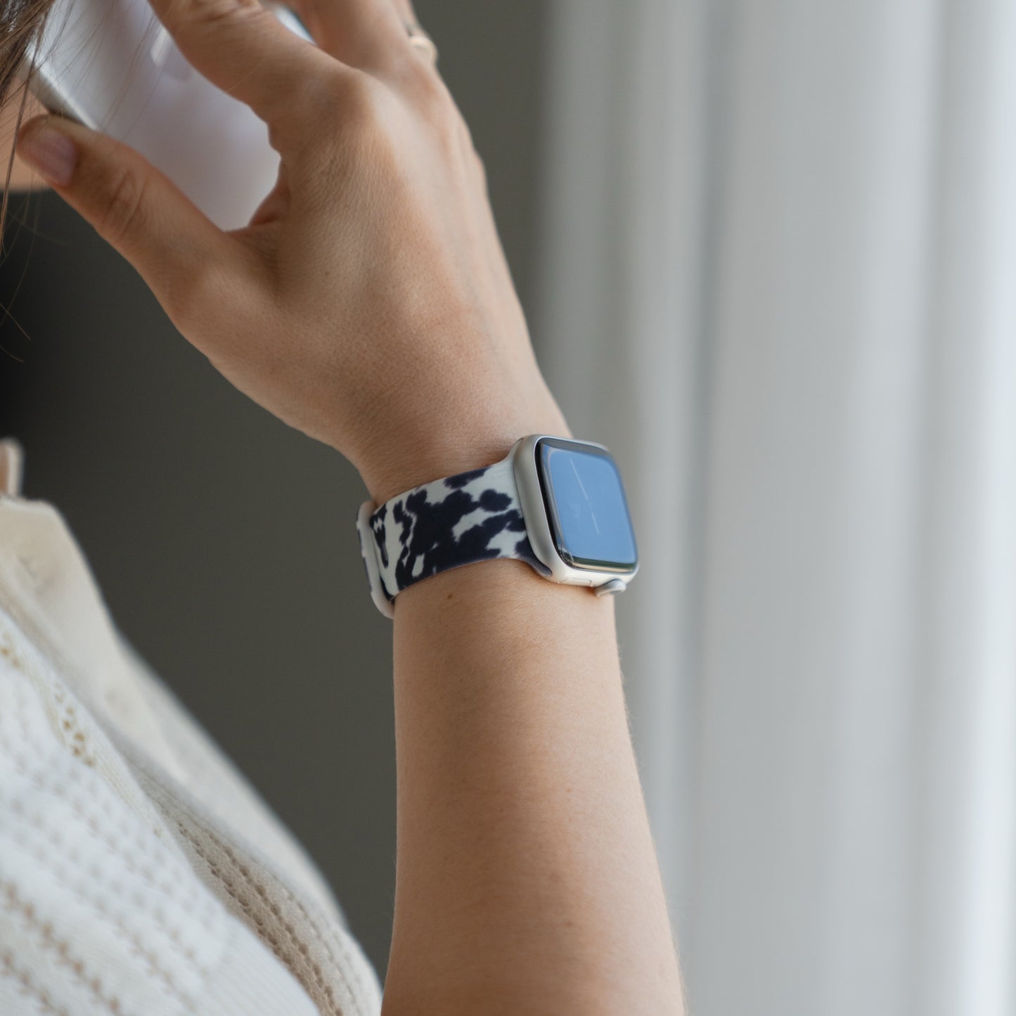 Jemand trägt ein „Kuhfell“-Apple-Watch-Armband von arktisband, dessen schwarz-weißes Muster einen sportlichen, stilvollen Akzent setzt, während er etwas nahe an sein Gesicht hält.