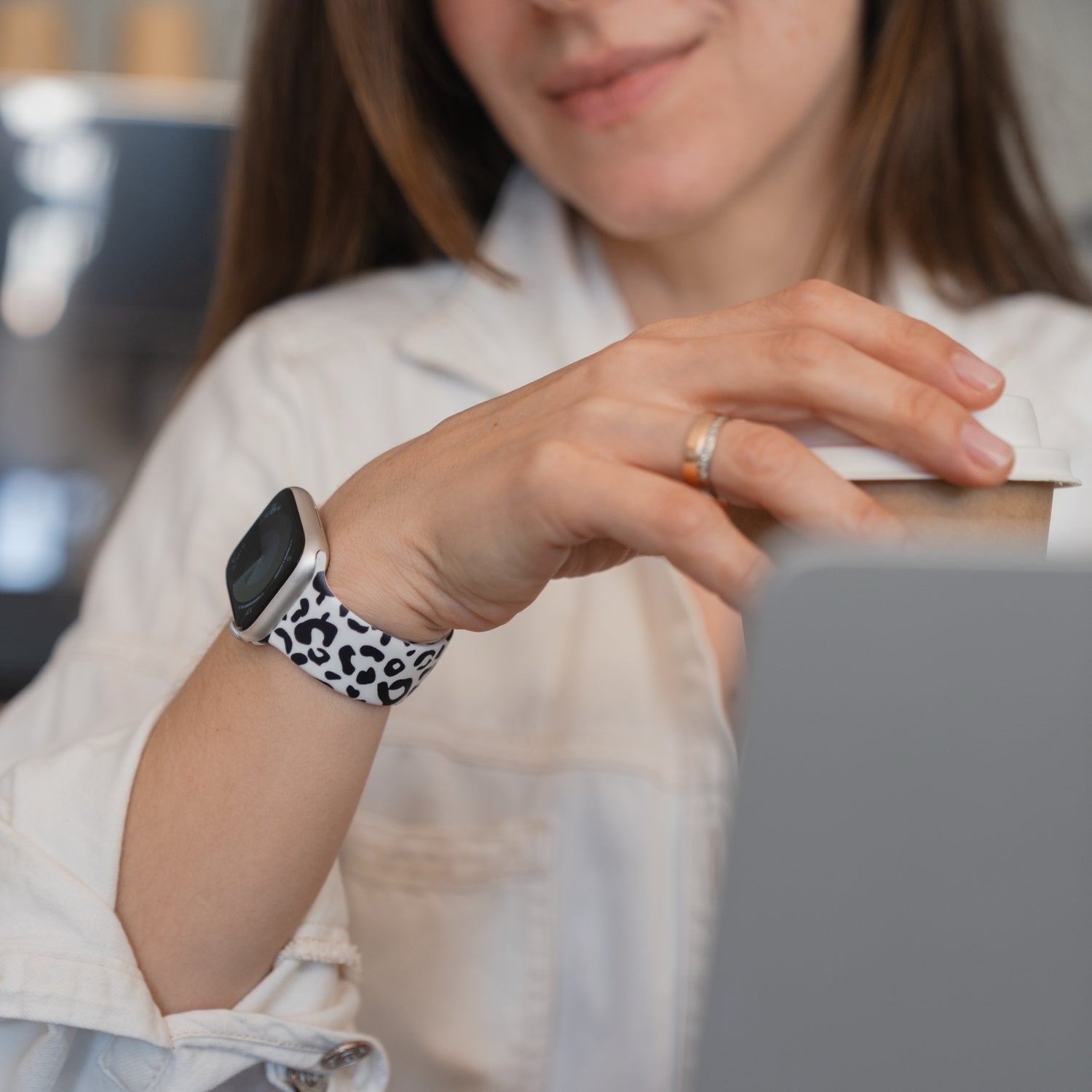 Eine Frau, die ein arktisband Snow Leopard Apple Watch Armband von arktisband trägt, sitzt an einem Schreibtisch und hält eine Kaffeetasse.