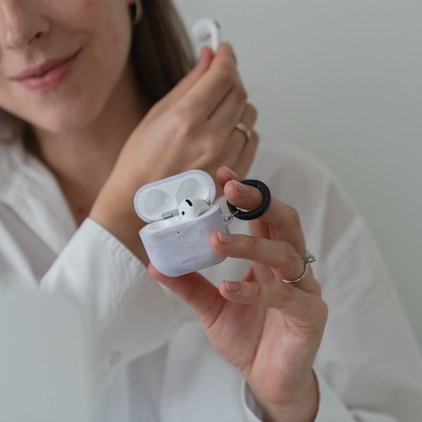 Eine Person, die eine Arktis AirPods 5 Hülle – Marble Flower mit einem schwarzen Ring hält.