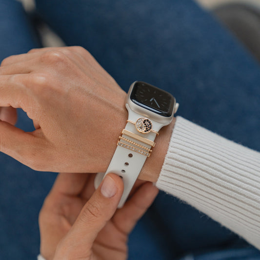 Diese Person in einem weißen gerippten Langarmshirt trägt eine Arktisband Apple Watch mit dem goldenen „Yin & Yang“-Charm und demonstriert moderne Eleganz und Stil.