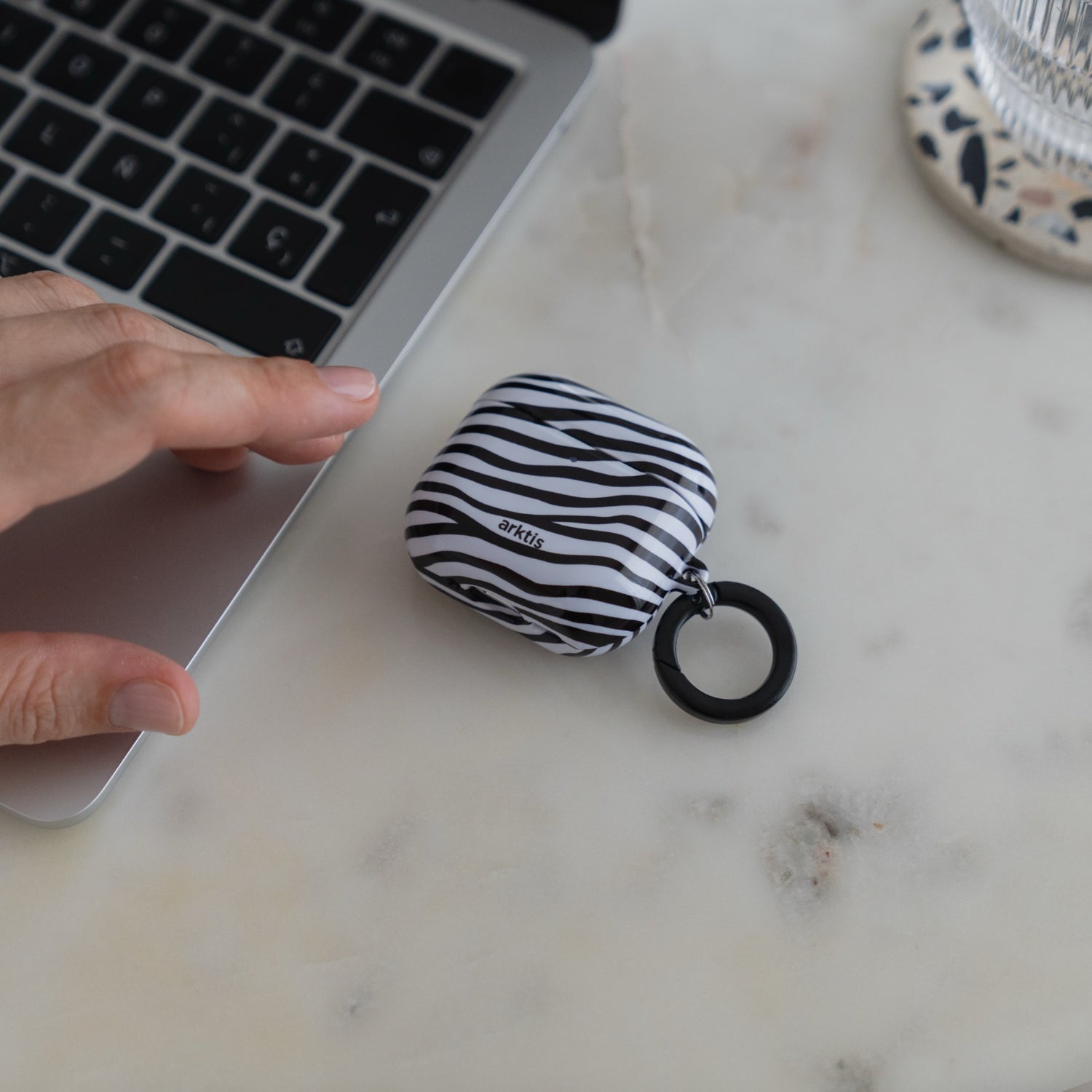 Arktis AirPods 5 Hülle – Zebra mit schwarz-weißem Streifenmuster und einer runden Befestigungsöse neben einem Laptop.