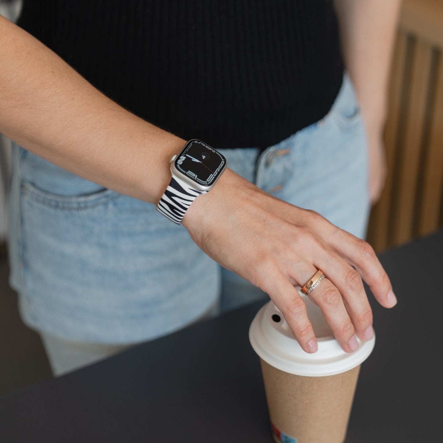 Jemand, der das arktisband Zebra Apple Watch Armband von arktisband trägt, hält einen Kaffeebecher zum Mitnehmen auf einem Tisch.
