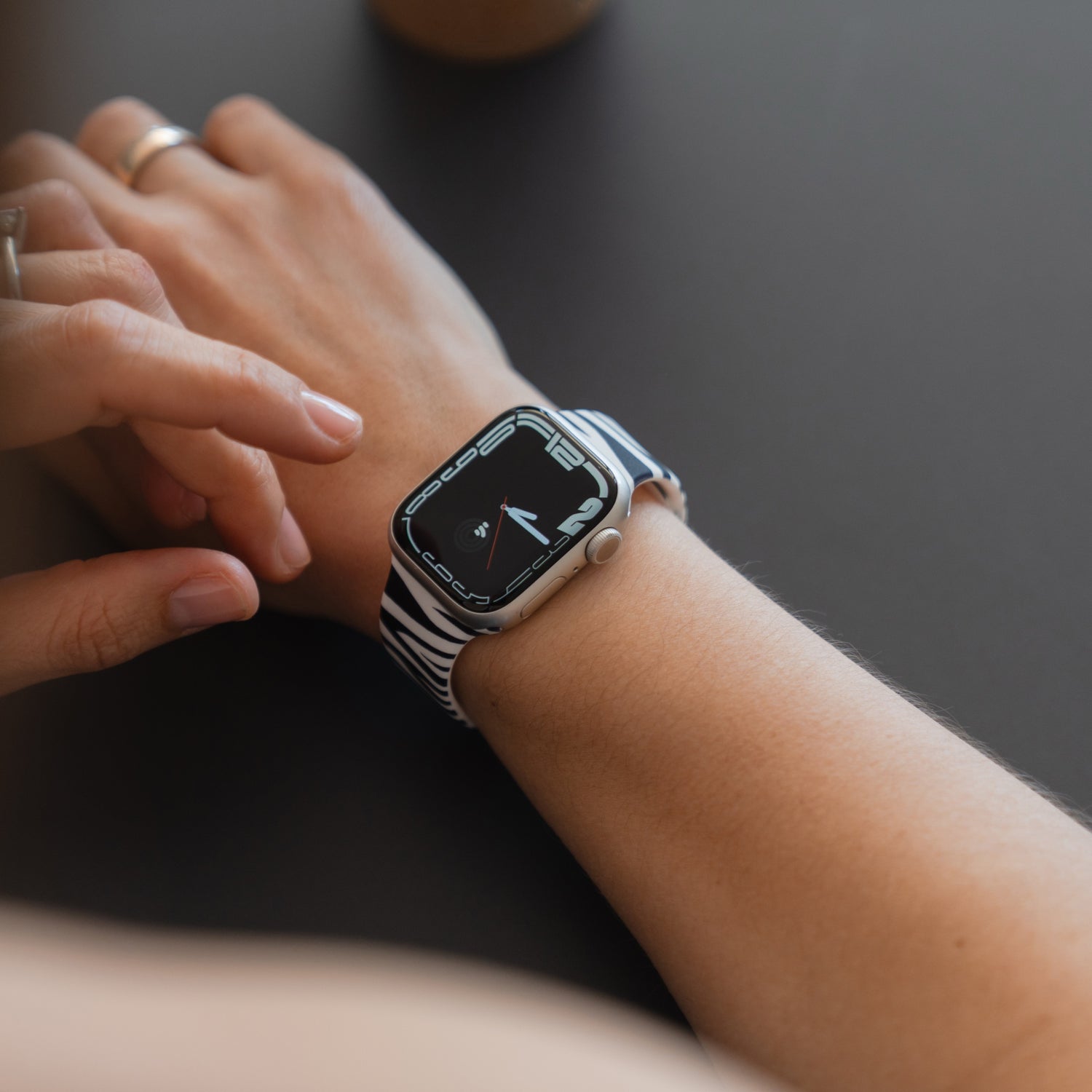 Eine Person, die ein arktisband Zebra Apple Watch Armband von arktisband trägt, berührt den Bildschirm der Uhr an einem dunklen Tisch.