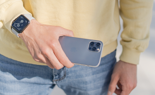 Eine Person in Jeans und gelbem Pullover hält ein iPhone mit einer ArktisPRO iPhone 13 Pro Hülle ULTRADÜNN und trägt eine Smartwatch am linken Handgelenk.