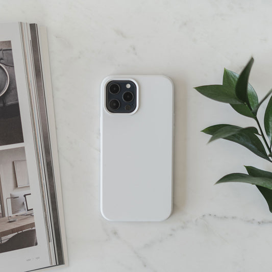 Das iCEO iPhone 12 Pro Max Silikon Case von iCEO liegt schlank auf einem weißen Marmortisch neben einem aufgeschlagenen Magazin und einer Grünpflanze – für stilvollen Schutz und kabelloses Laden.